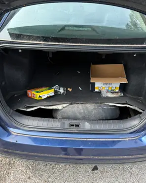 Sedan trunk with loose packaging, debris and dirt worked into the carpet