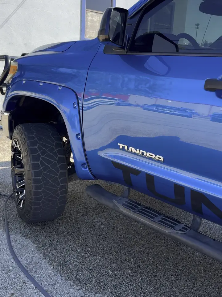 Blue Toyota Tundra on a lot after an exterior detail, paint reflecting and the wash hose still on the ground